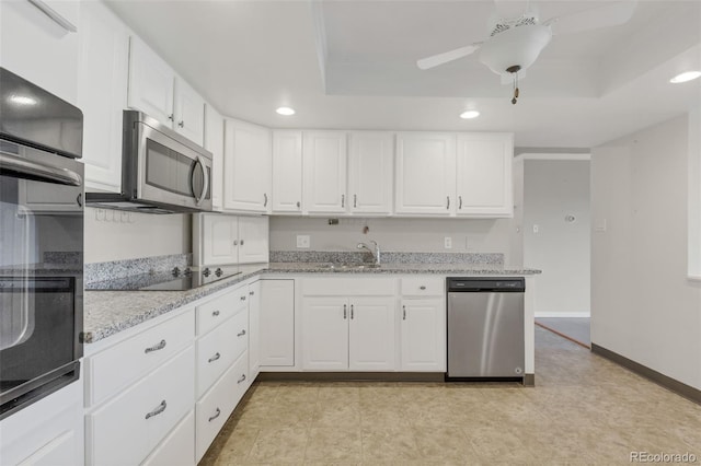 kitchen featuring appliances with stainless steel finishes, a tray ceiling, white cabinets, recessed lighting, and a sink