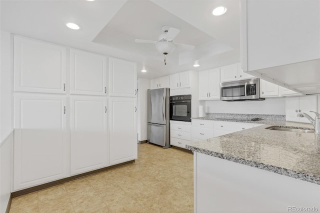 kitchen with black appliances, a sink, a raised ceiling, light stone counters, and white cabinetry