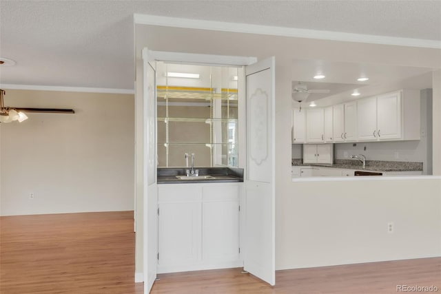 kitchen featuring crown molding, a sink, white cabinetry, light wood-style flooring, and a textured ceiling