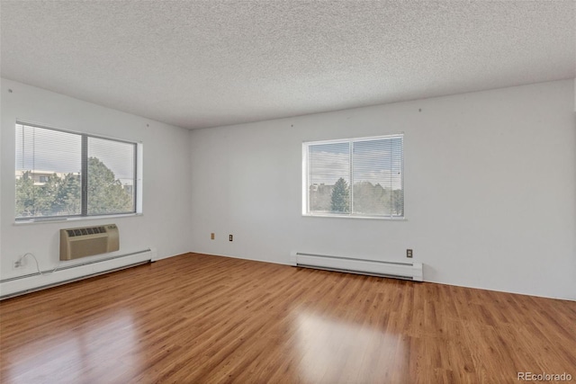 unfurnished room featuring a baseboard heating unit, wood finished floors, a textured ceiling, and a wall mounted air conditioner