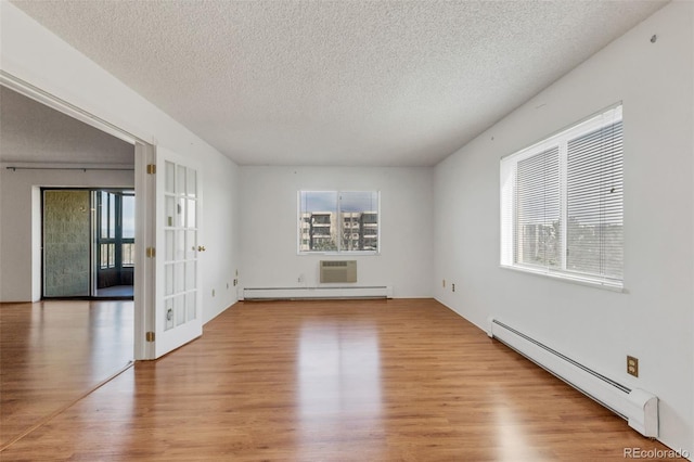 unfurnished room with baseboard heating, wood finished floors, plenty of natural light, and a textured ceiling