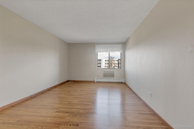 empty room with a baseboard radiator, light wood-type flooring, baseboards, and a textured ceiling