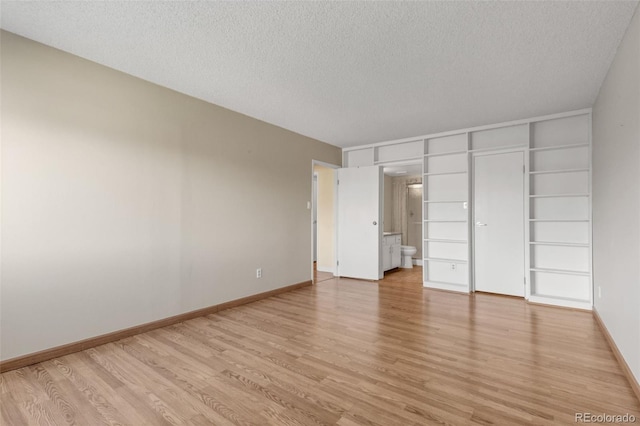 unfurnished bedroom featuring a textured ceiling, light wood-style flooring, connected bathroom, and baseboards