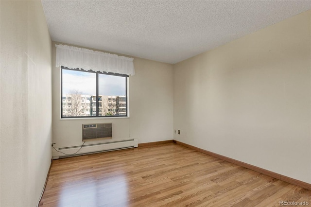 unfurnished room with baseboard heating, light wood-type flooring, a textured ceiling, baseboards, and a wall mounted air conditioner