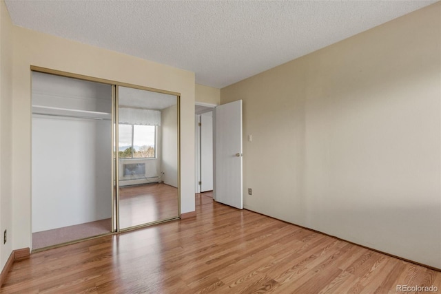 unfurnished bedroom featuring light wood finished floors, a closet, a textured ceiling, and a baseboard radiator