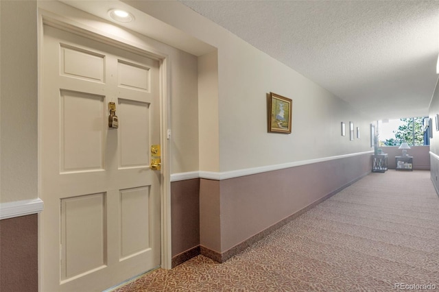hallway with carpet floors, a textured ceiling, and baseboards