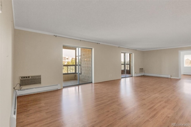empty room featuring ornamental molding, baseboard heating, light wood-style flooring, and baseboards