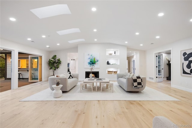 living room with light wood-style flooring, lofted ceiling with skylight, visible vents, baseboards, and recessed lighting