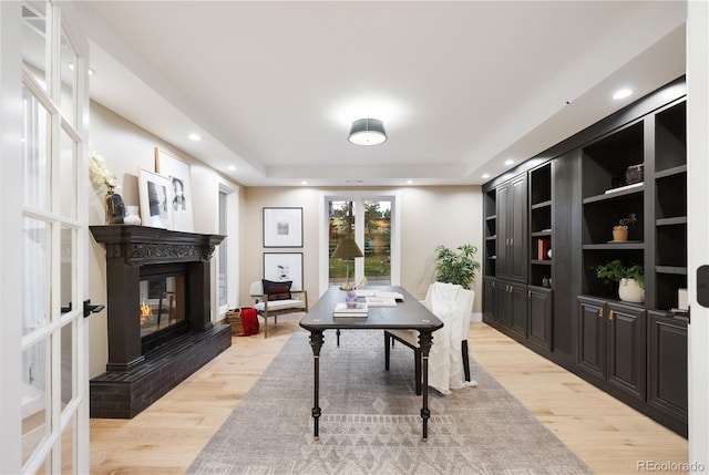 office featuring a tray ceiling, light wood-type flooring, a glass covered fireplace, and recessed lighting