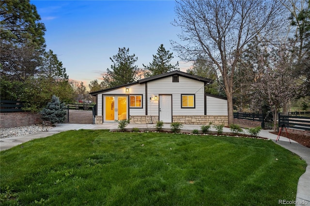 view of front of home with a yard, fence, and stone siding