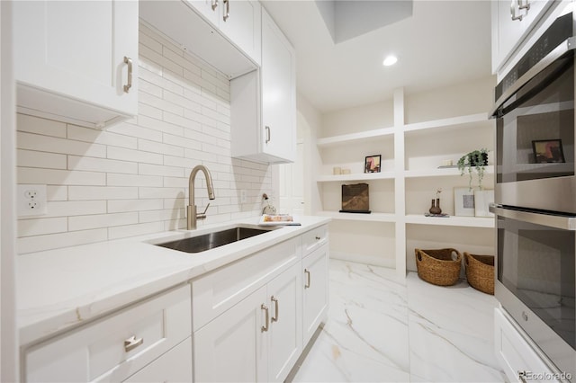 kitchen featuring white cabinetry, marble finish floor, double oven, and a sink