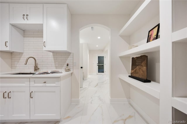 kitchen featuring baseboards, marble finish floor, arched walkways, light countertops, and white cabinets