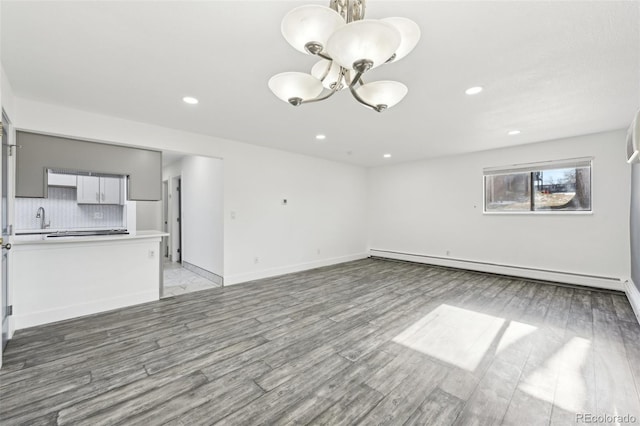 unfurnished living room featuring a baseboard radiator, sink, a notable chandelier, and light hardwood / wood-style floors