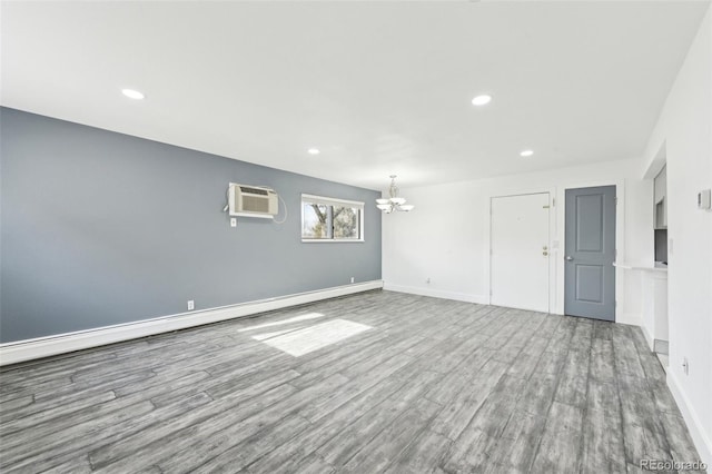 unfurnished living room with hardwood / wood-style floors, a wall unit AC, a chandelier, and a baseboard heating unit