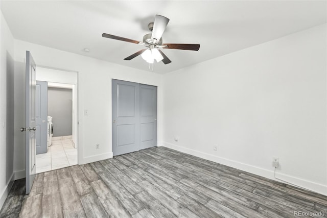 unfurnished bedroom featuring washer / clothes dryer, light hardwood / wood-style floors, a closet, and ceiling fan