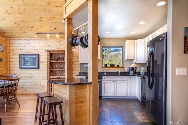 kitchen featuring a kitchen bar, dark stone counters, white cabinets, and freestanding refrigerator