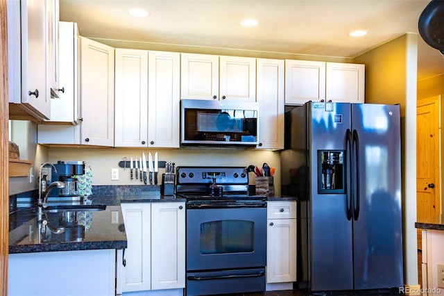 kitchen featuring dark stone countertops, appliances with stainless steel finishes, white cabinets, and a sink