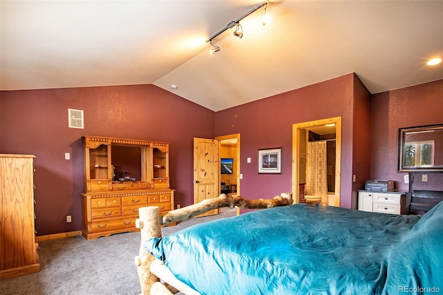 carpeted bedroom with rail lighting, a textured wall, vaulted ceiling, ensuite bath, and baseboards