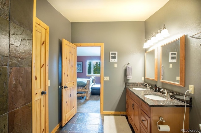 bathroom with double vanity, a sink, stone tile flooring, and baseboards