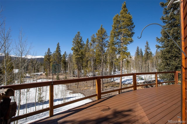 snow covered deck featuring a forest view and a mountain view