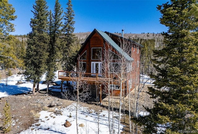 snow covered house with a wooded view and a wooden deck