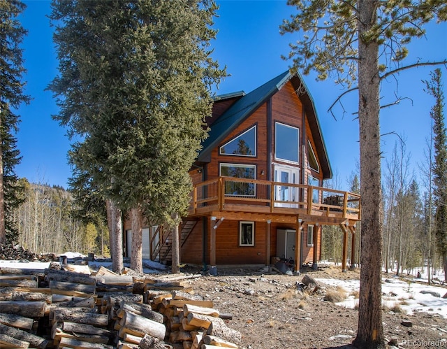 back of property featuring a forest view, a wooden deck, and stairs