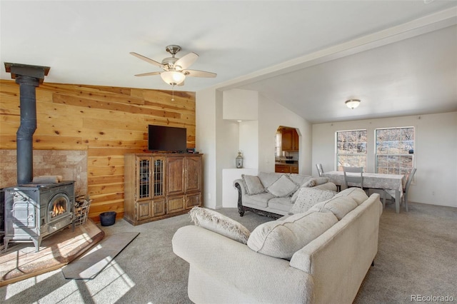 living room with light carpet, ceiling fan, a wood stove, vaulted ceiling, and wood walls