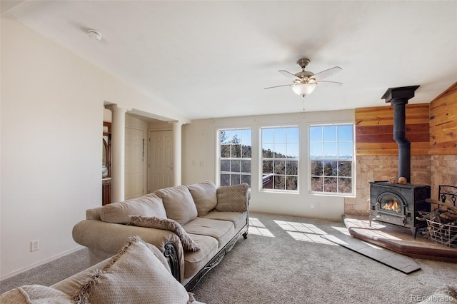 carpeted living room featuring a wood stove, ceiling fan, wooden walls, and decorative columns