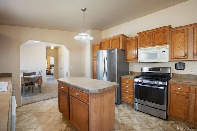 kitchen featuring arched walkways, stainless steel appliances, brown cabinetry, and a kitchen island