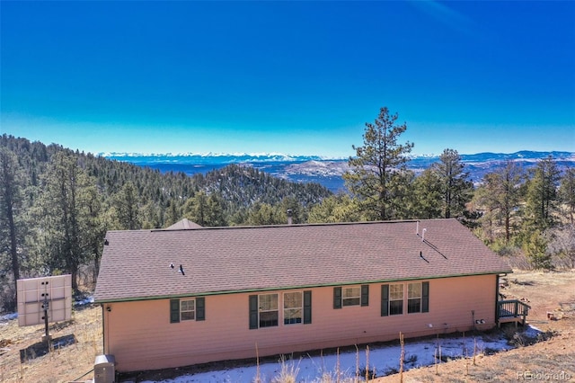 view of side of home with a forest view, roof with shingles, and a mountain view