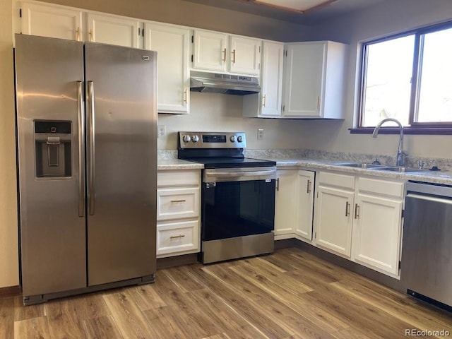 kitchen with light stone countertops, stainless steel appliances, sink, white cabinets, and light hardwood / wood-style floors