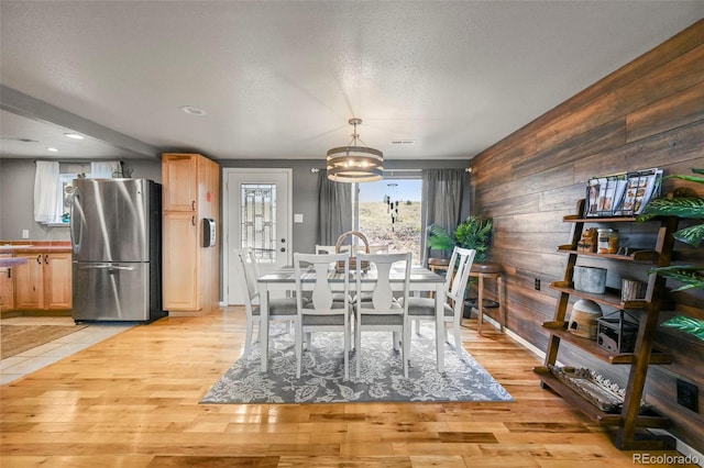 dining space featuring a textured ceiling, wood walls, a chandelier, and light hardwood / wood-style flooring