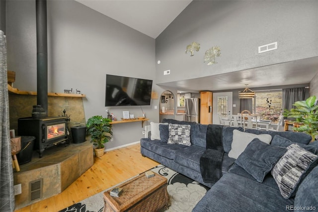 living room with hardwood / wood-style flooring, high vaulted ceiling, and a wood stove