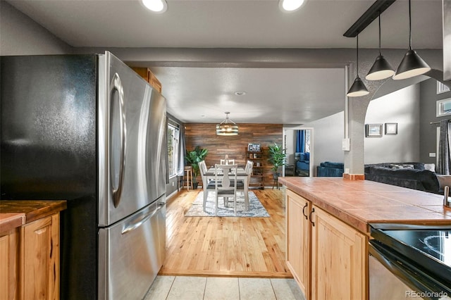 kitchen featuring pendant lighting, stainless steel fridge, wooden walls, and tile counters