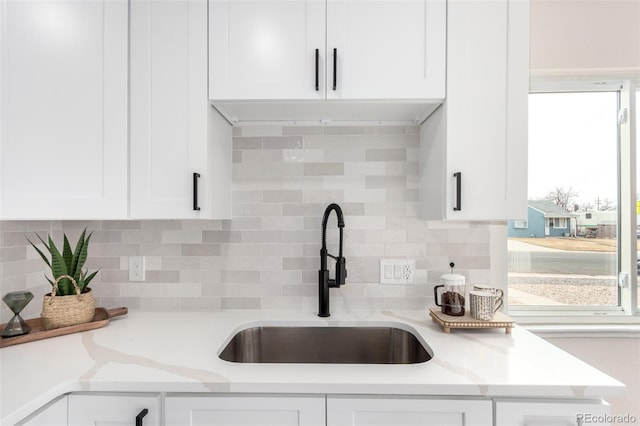 kitchen featuring a sink, white cabinetry, light stone counters, and tasteful backsplash