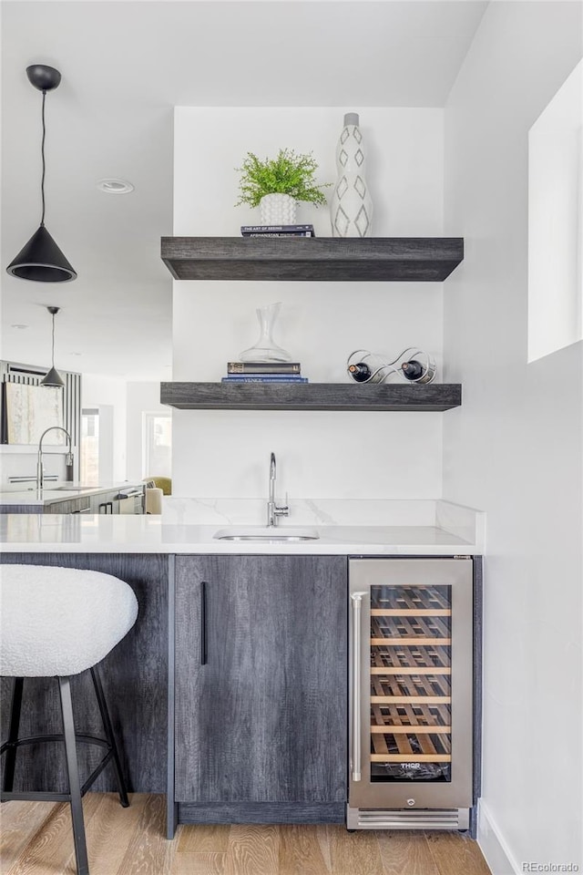 bar featuring wine cooler, sink, hanging light fixtures, and wood-type flooring