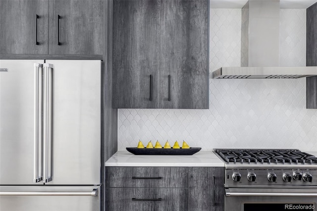 kitchen featuring high end appliances, wall chimney range hood, light stone counters, and tasteful backsplash