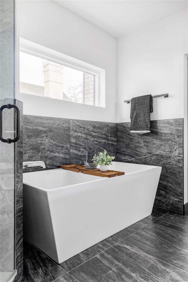 bathroom with a bathtub, a healthy amount of sunlight, and tile walls