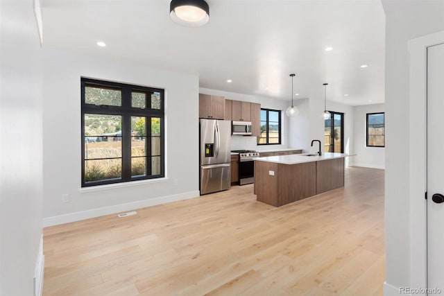 kitchen featuring appliances with stainless steel finishes, hanging light fixtures, light hardwood / wood-style floors, and an island with sink