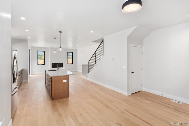 kitchen with a center island, sink, hanging light fixtures, stainless steel refrigerator, and light hardwood / wood-style flooring