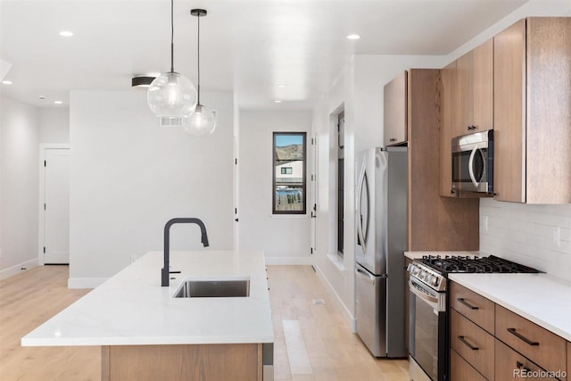 kitchen featuring hanging light fixtures, sink, a kitchen island with sink, light hardwood / wood-style flooring, and stainless steel appliances