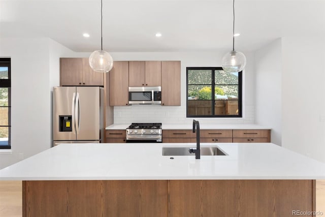 kitchen with a center island with sink, sink, stainless steel appliances, and decorative light fixtures