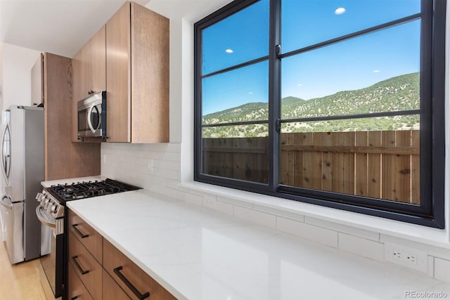 kitchen featuring a mountain view, light stone counters, light hardwood / wood-style flooring, backsplash, and appliances with stainless steel finishes