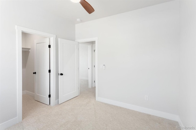 unfurnished bedroom featuring light carpet, a closet, ceiling fan, and a spacious closet