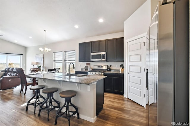 kitchen with sink, appliances with stainless steel finishes, a kitchen island with sink, hanging light fixtures, and stone countertops