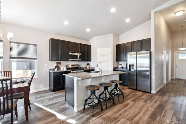 kitchen with pendant lighting, sink, a kitchen island with sink, stainless steel appliances, and light stone counters