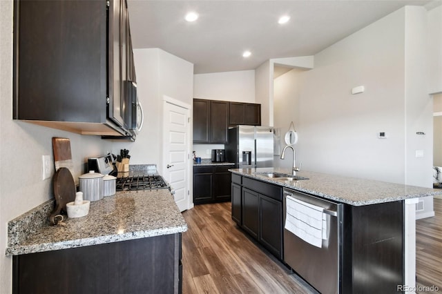 kitchen with stainless steel appliances, an island with sink, light stone countertops, and sink