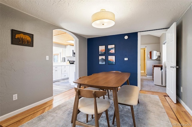 470 Bear Creek Rd, Colorado Springs, CO 80906 - dining space with light wood-style floors, baseboards, a textured wall, arched walkways, and a textured ceiling