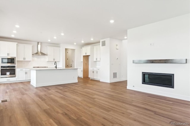 8346 Cokedale Cir, Littleton, CO 80125 - kitchen with appliances with stainless steel finishes, wall chimney range hood, open floor plan, recessed lighting, and light wood-style flooring