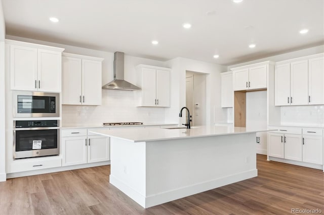 8346 Cokedale Cir, Littleton, CO 80125 - kitchen with appliances with stainless steel finishes, wall chimney exhaust hood, a kitchen island with sink, decorative backsplash, and light wood-style floors